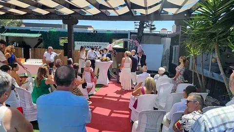 Un grupo de personas están sentadas en sillas viendo una ceremonia de boda.