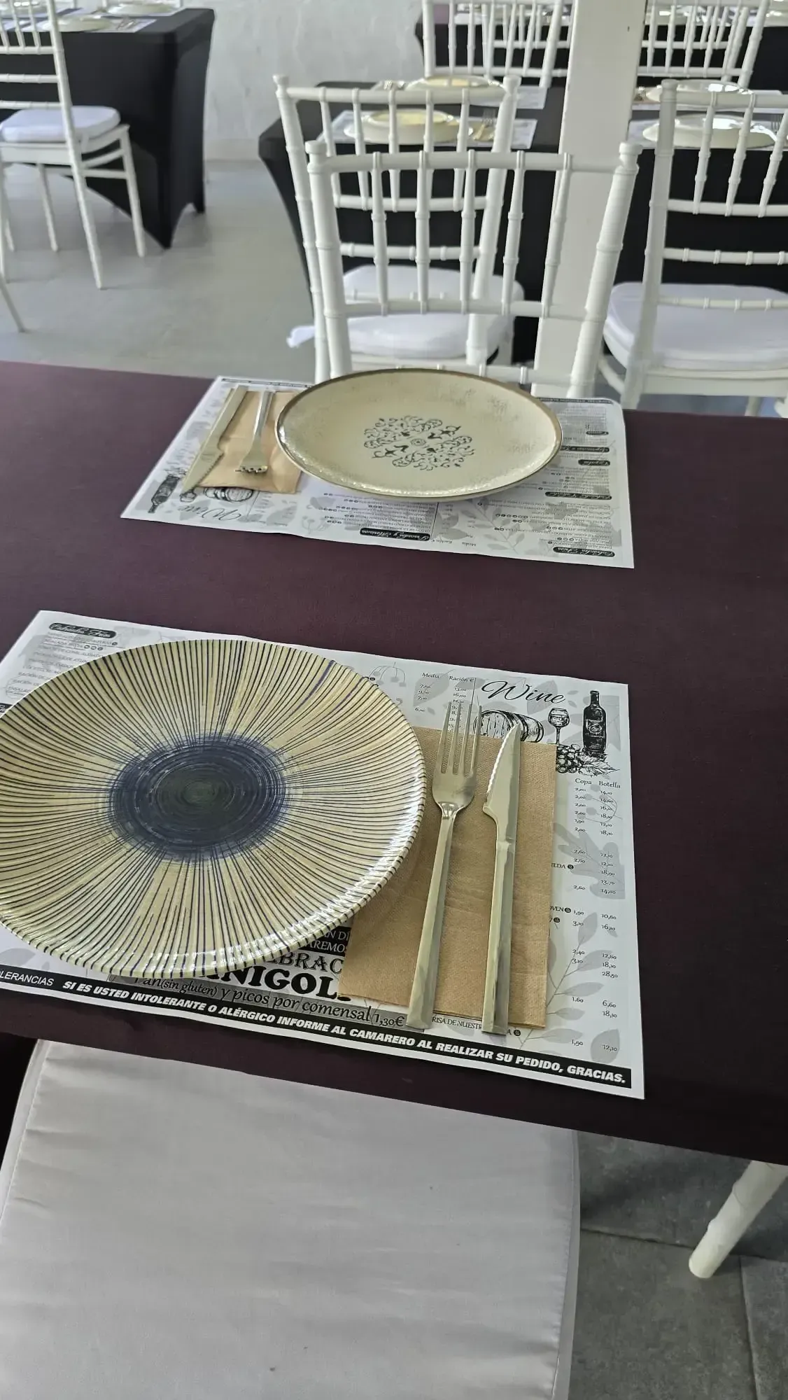 Prepara las mesas del comedor con manteles individuales y platos tejidos en un restaurante luminoso.