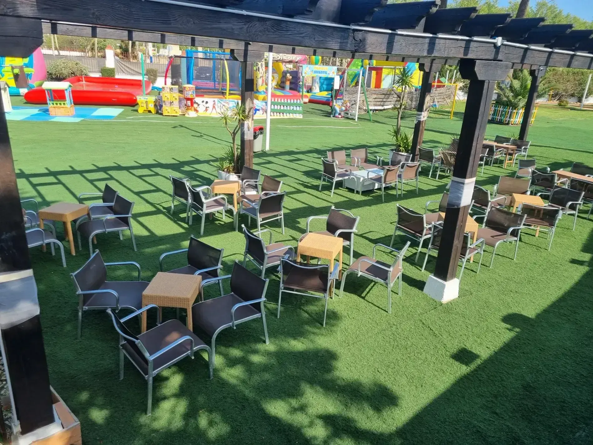 Una fila de mesas y sillas bajo una pérgola en un parque.