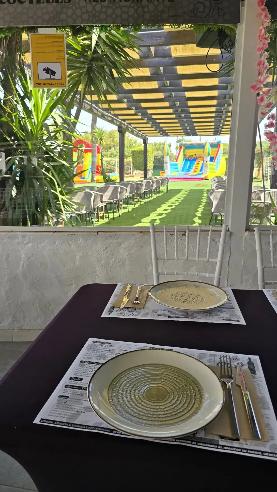 Mesa preparada en un patio sombreado con vistas a un jardín luminoso y una pérgola.