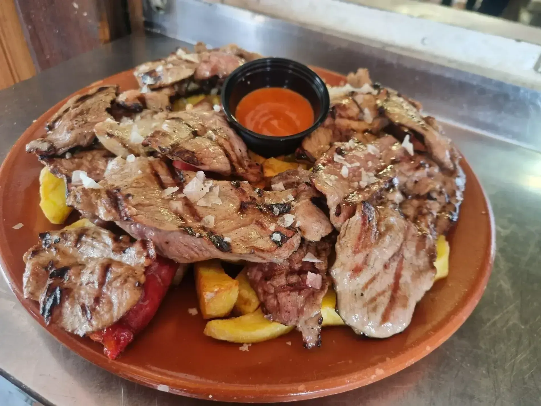 Un plato de carne y verduras con salsa para mojar sobre una mesa.