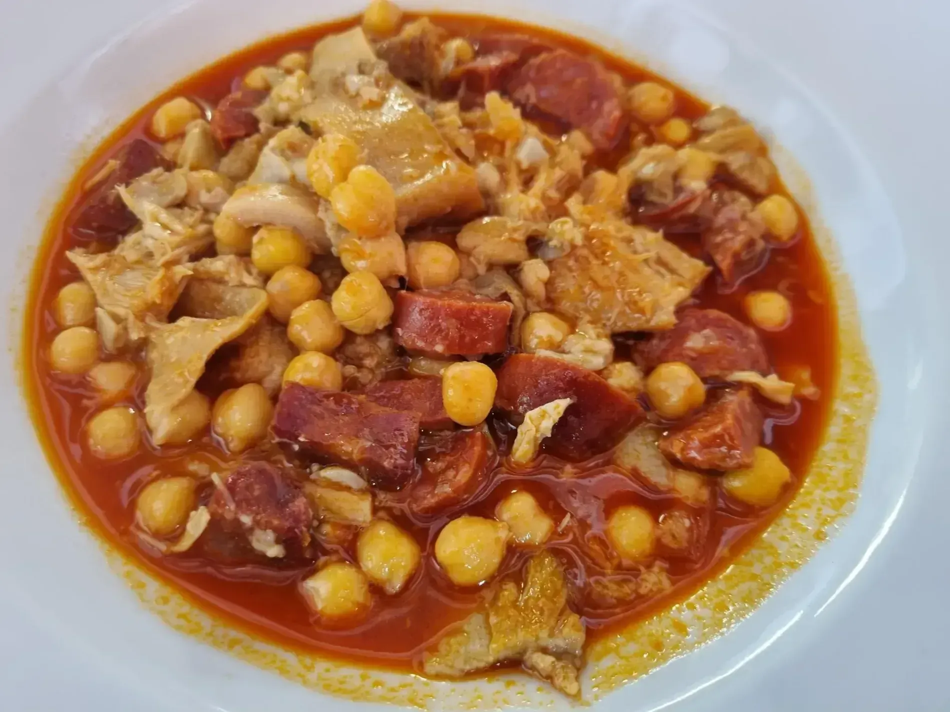 Un tazón de sopa con garbanzos y carne en un plato blanco.