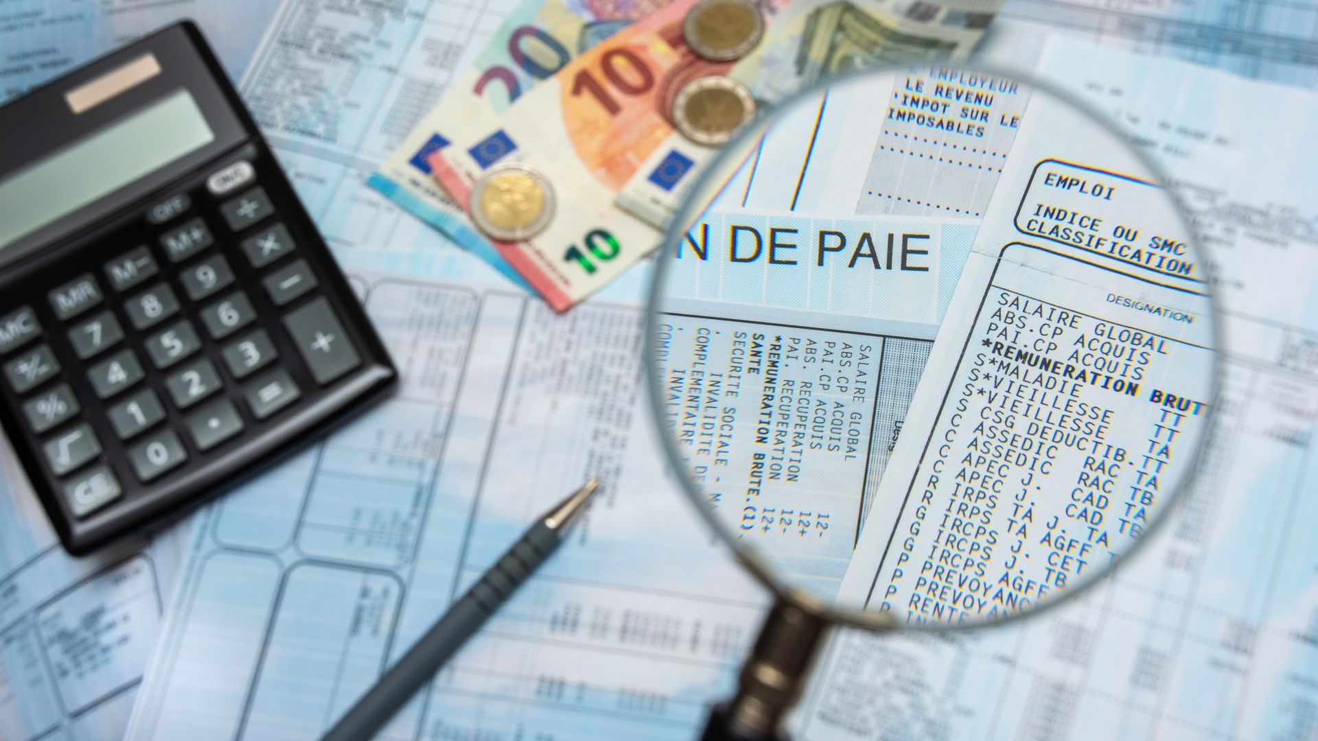 Bulletin de paie à la loupe, avec argent liquide en euros, calculette et stylo.