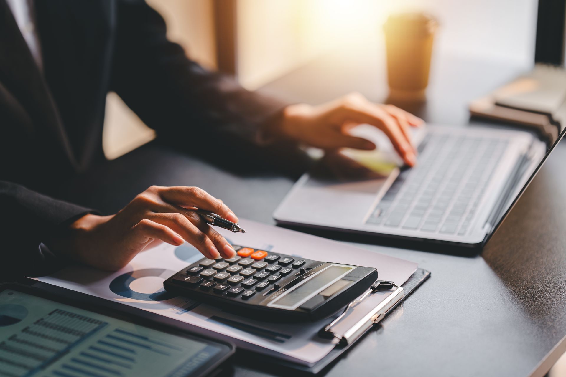Une femme devant son ordinateur tapant sur une calculatrice posée sur des dossiers avec diagrammes.