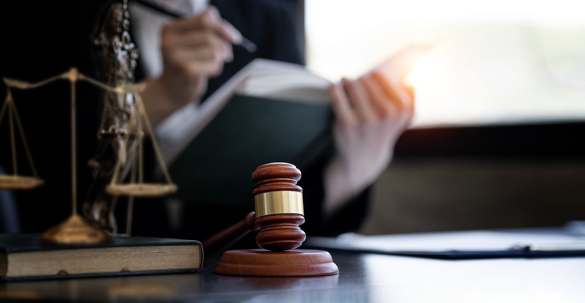 Marteau en bois sur un bureau avec une balance de justice et une avocate en fond.