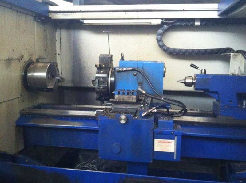Máquina industrial en un taller, con un torno azul y piezas metálicas montadas sobre la bancada.