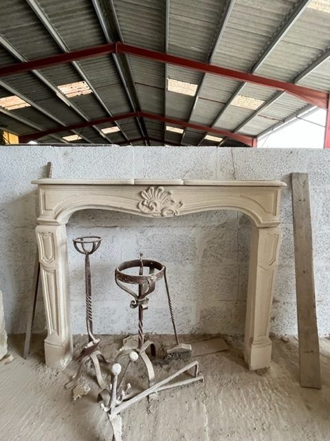 Une cheminée en pierre calcaire aux détails ornementaux, accompagnée de bougeoirs en métal, se trouve dans un bâtiment au toit métallique.