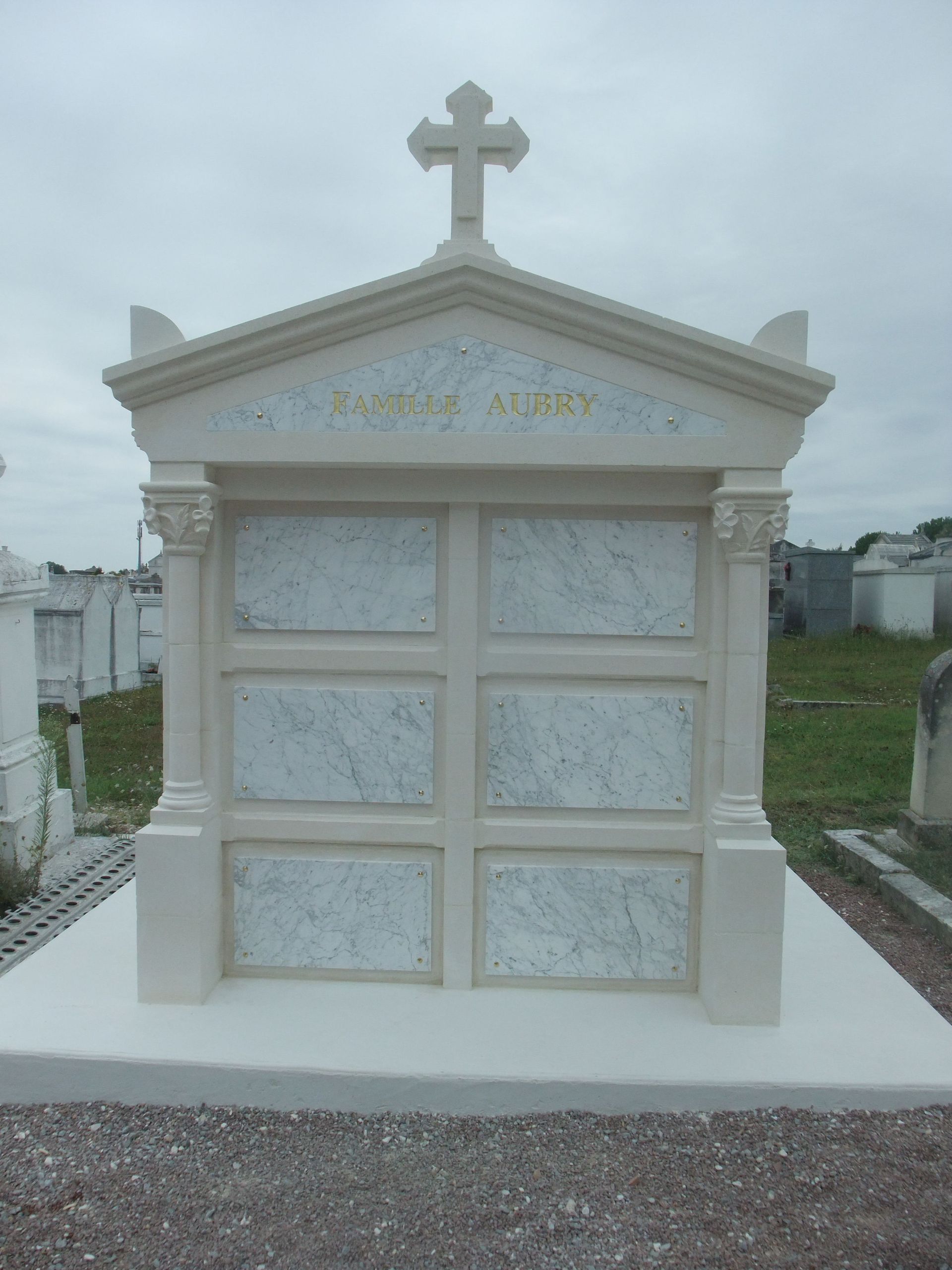 Petit mausolée blanc surmonté d'une croix dans un cimetière