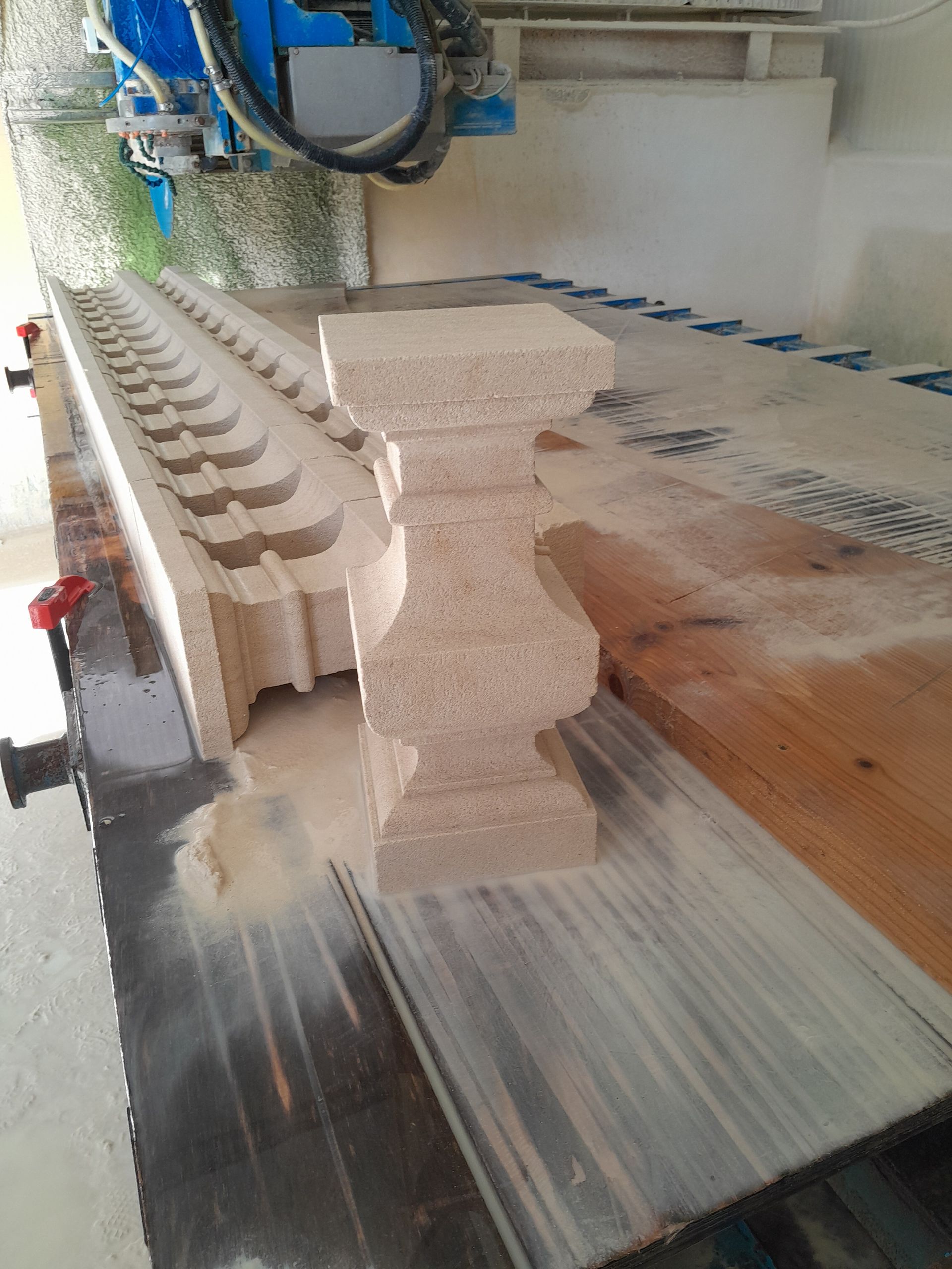Machine à sculpter la pierre en train de découper des blocs de mousse beige empilés, recouverts de poussière, sur une table d'atelier