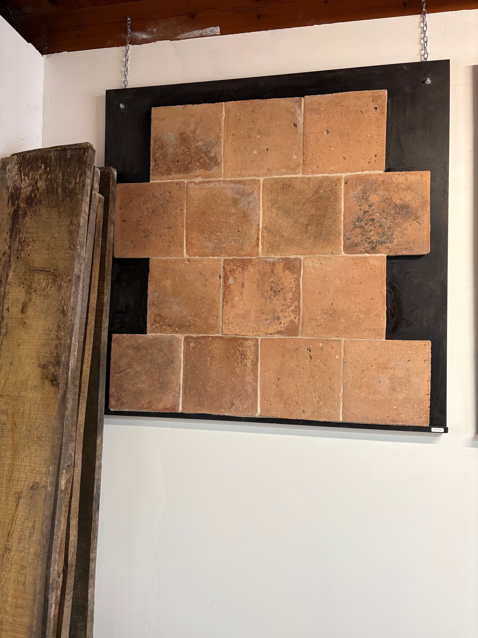Panneau mural à cadre noir avec échantillons de pierre ou de carrelage beige, fixé au-dessus d'un mur blanc.