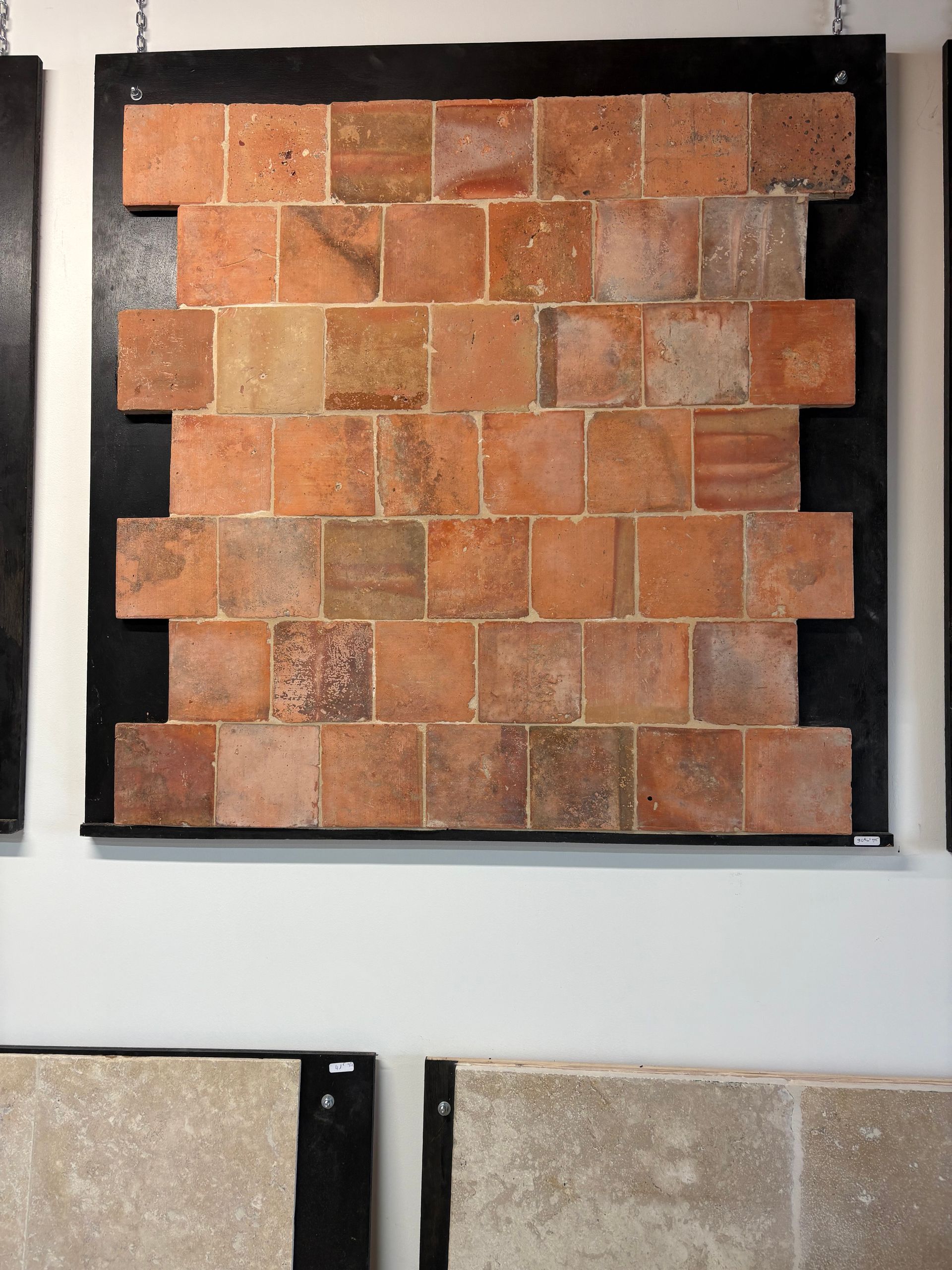 Échantillon de carreau de pierre brun orangé monté dans un cadre d'exposition, avec des fragments d'échantillons de carreaux visibles en dessous