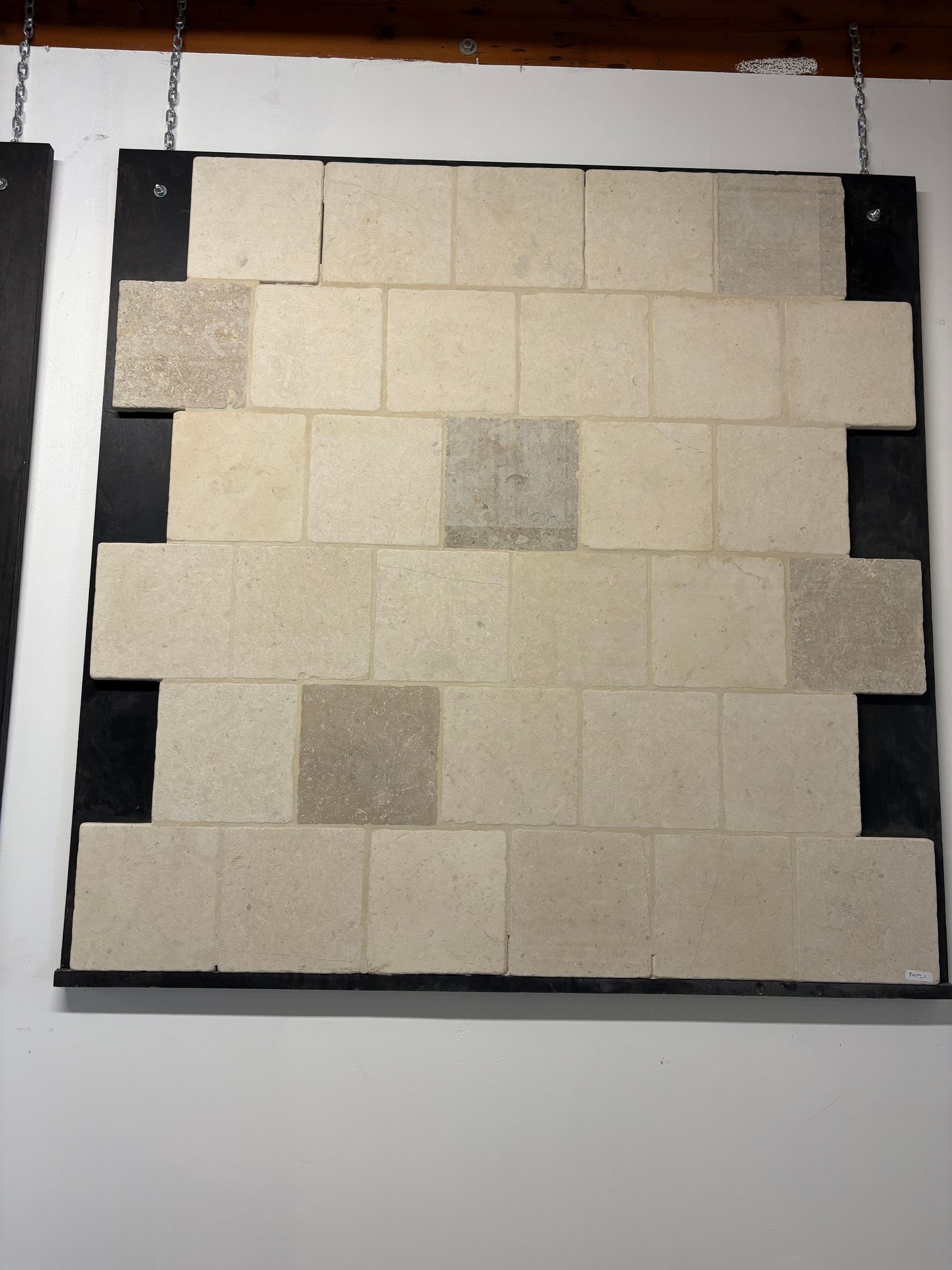 Petit panneau d'échantillons de carrelage mural crème et gris avec quelques carreaux d'accent plus foncés sur fond noir.