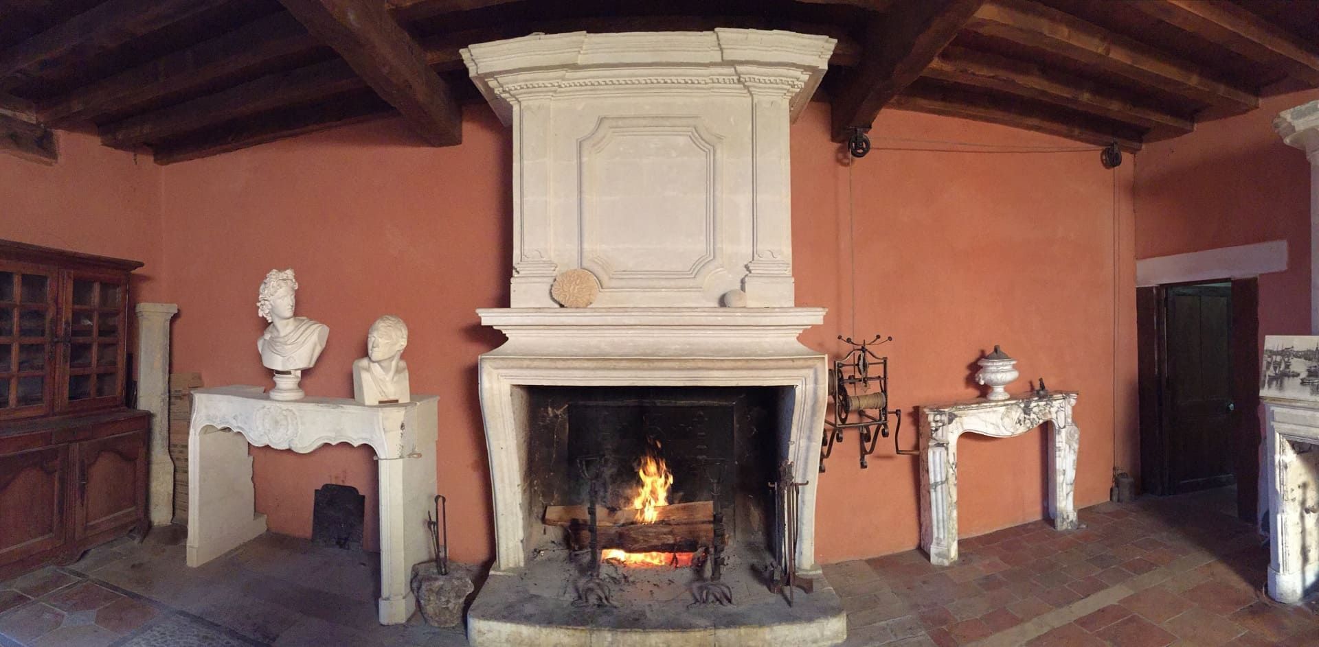 Une cheminée avec un feu qui crépite dans une pièce aux murs rouges et au décor en marbre.