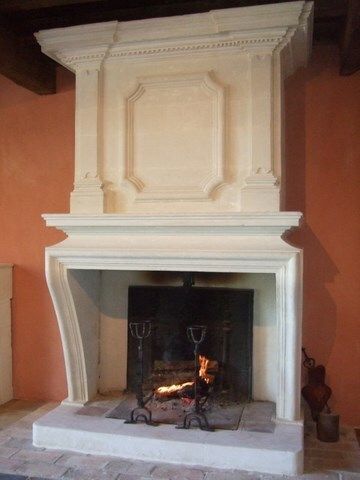 Cheminée avec manteau blanc sculpté ; flammes dans le foyer.