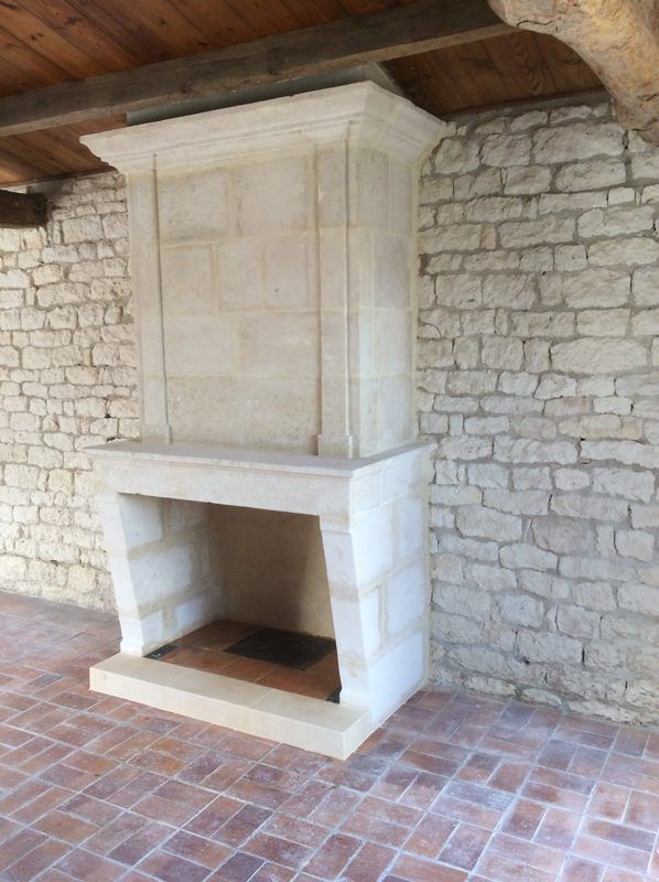 Cheminée en pierre contre un mur de briques, sol en briques rouges, poutres apparentes au plafond.