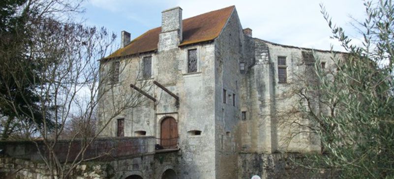 Château en pierre au toit de tuiles rouges, pont-levis et muraille de pierre. Ciel nuageux.