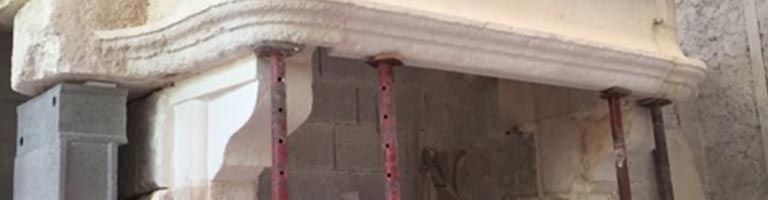 Détail architectural : structure en pierre sculptée soutenue par des étais métalliques rouges lors de la restauration.