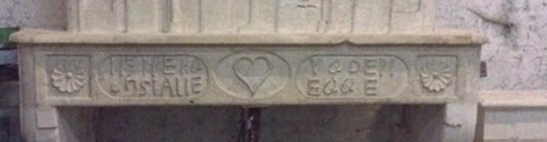 Manteau de cheminée en pierre sculptée avec inscriptions et motif de cœur.