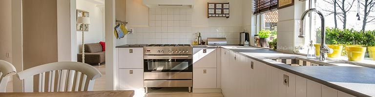 Cuisine avec placards blancs, appareils électroménagers en acier inoxydable et fenêtre avec plantes.