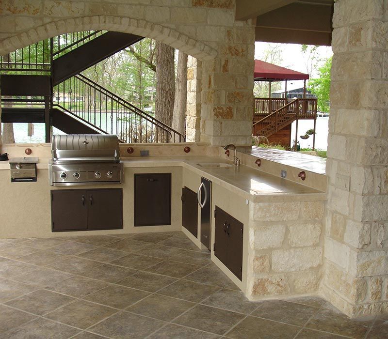Cuisine extérieure avec comptoirs en pierre, armoires brunes et barbecue.