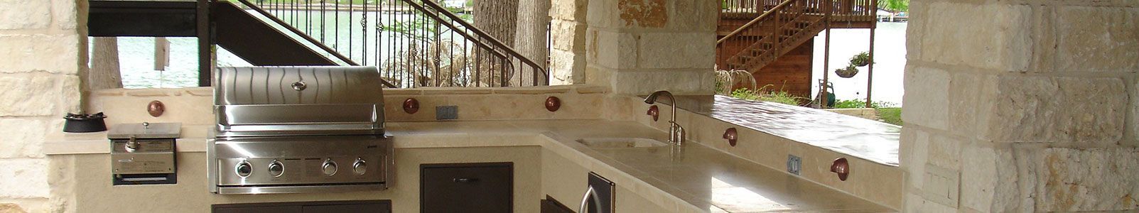 Cuisine extérieure avec barbecue en acier inoxydable, placards et entourage en pierre.