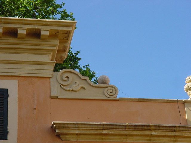 Gros plan sur la façade d'un immeuble couleur pêche, ornée de moulures décoratives, avec un ciel bleu au-dessus.