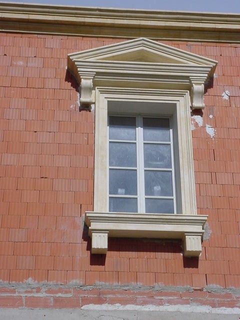 Petite fenêtre à encadrement blanc sur un mur de briques rouges avec un fronton et un appui décoratifs