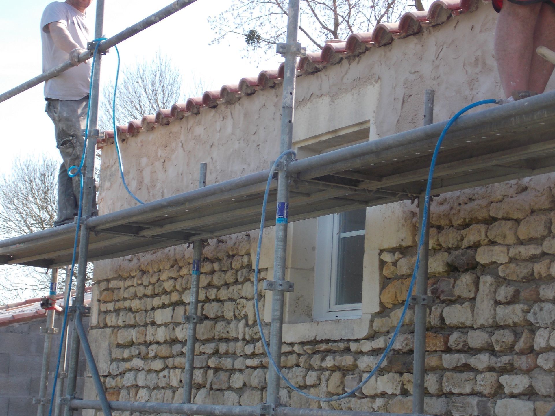 Échafaudages autour d'un bâtiment en pierre en rénovation, avec des ouvriers de part et d'autre.