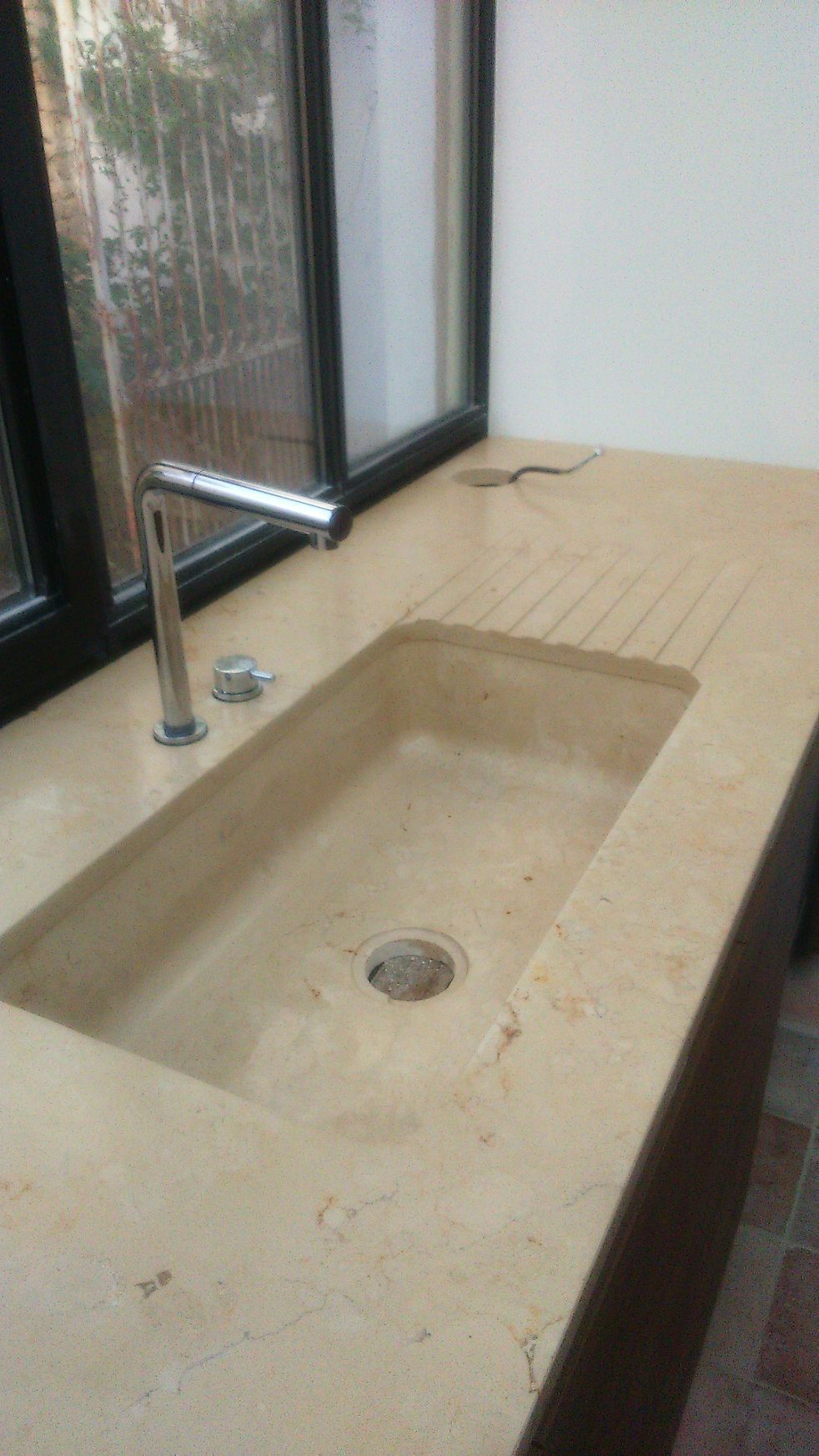 Comptoir de salle de bain en pierre avec vasque rectangulaire et robinet chromé à côté d'une fenêtre