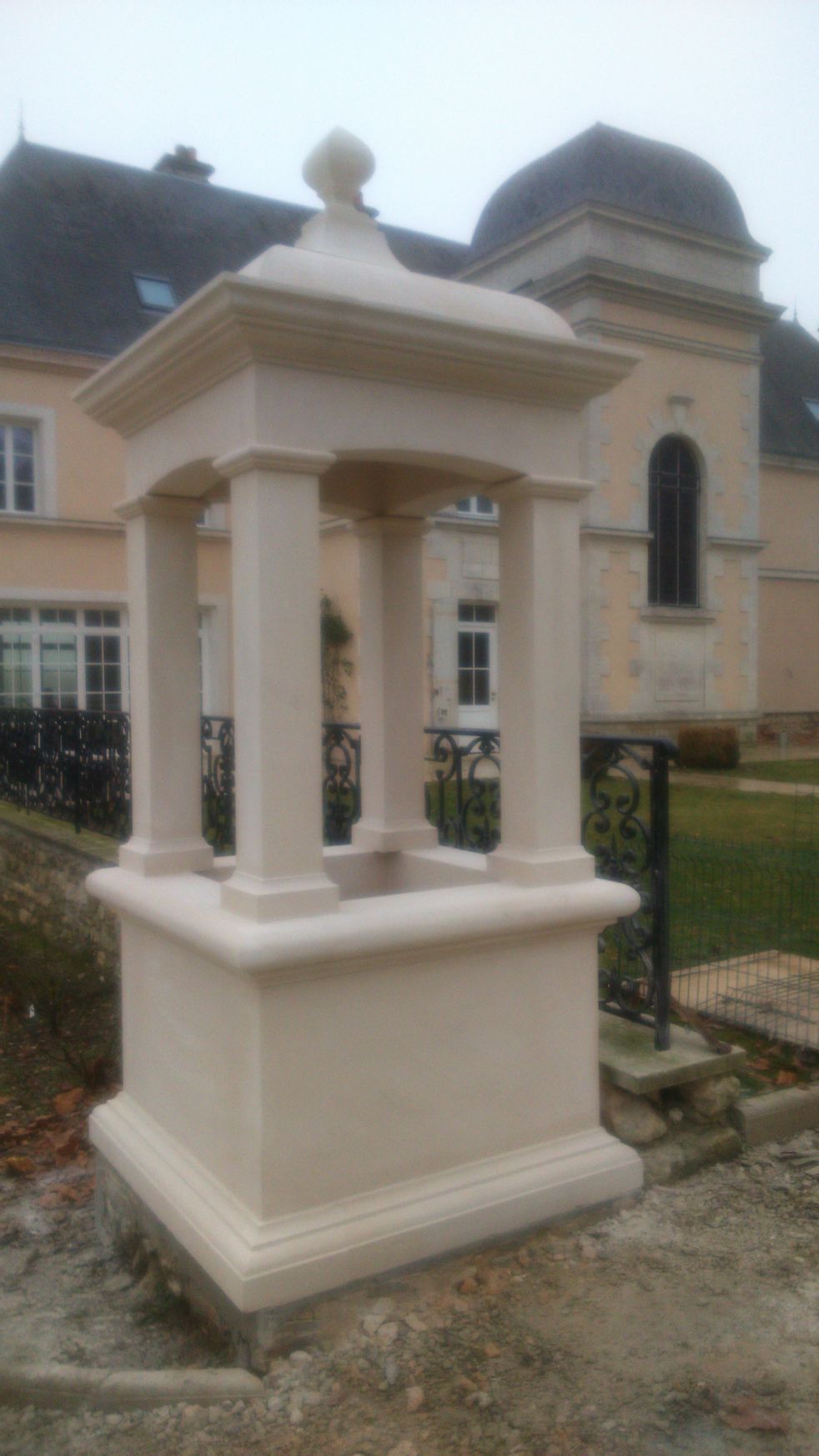 Lanterne décorative blanche de jardin sur un piédestal devant un bâtiment beige et une clôture noire