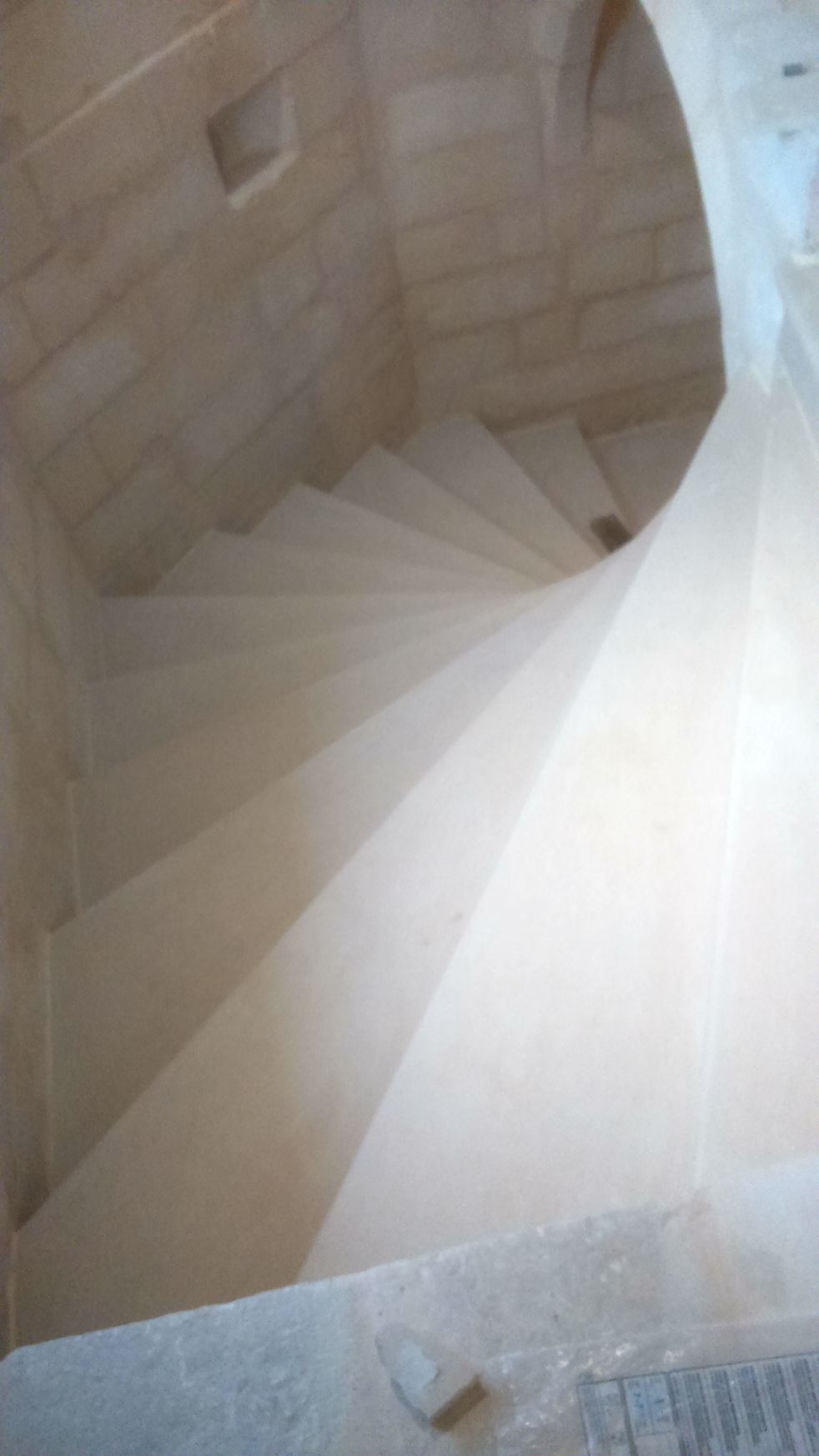 Escalier en pierre en colimaçon descendant à l'intérieur d'une tour beige, vu d'en haut