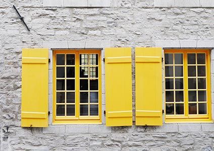 Volets et encadrements de fenêtres jaunes sur un mur de pierre grise.