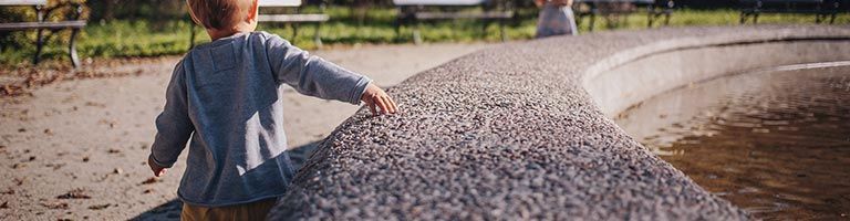 Un jeune enfant marche vers un mur de pierre incurvé à l'extérieur.