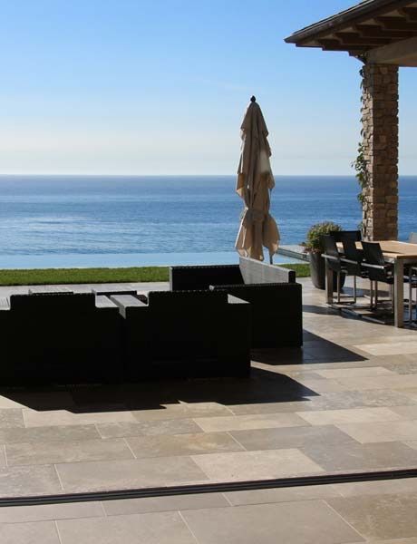 Patio avec vue sur l'océan, mobilier de jardin noir, parasol fermé et terrasse carrelée au bord d'une piscine.