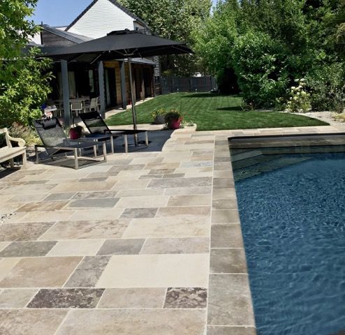 Terrasse moderne dans un jardin avec piscine, chaises longues, parasol noir et une maison en arrière-plan.