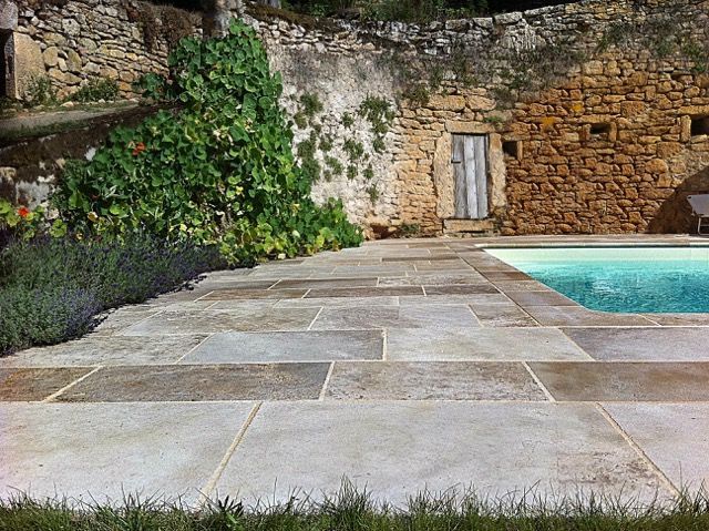 Terrasse en pierre bordant une piscine turquoise, avec un muret rustique en pierre et un coin recouvert de lierre