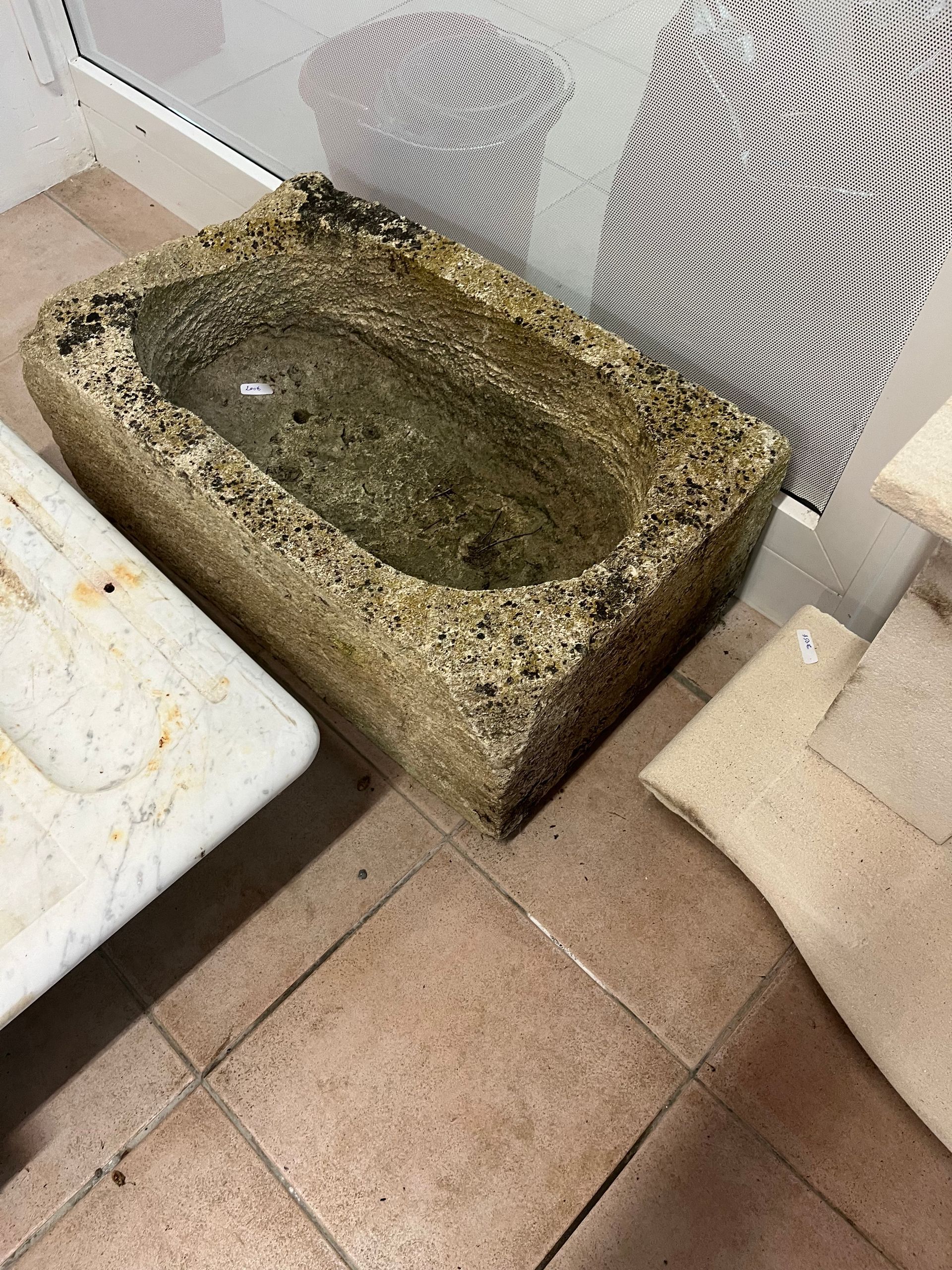 Bassin en pierre moussue rempli d'eau stagnante à côté de carreaux empilés dans un atelier.