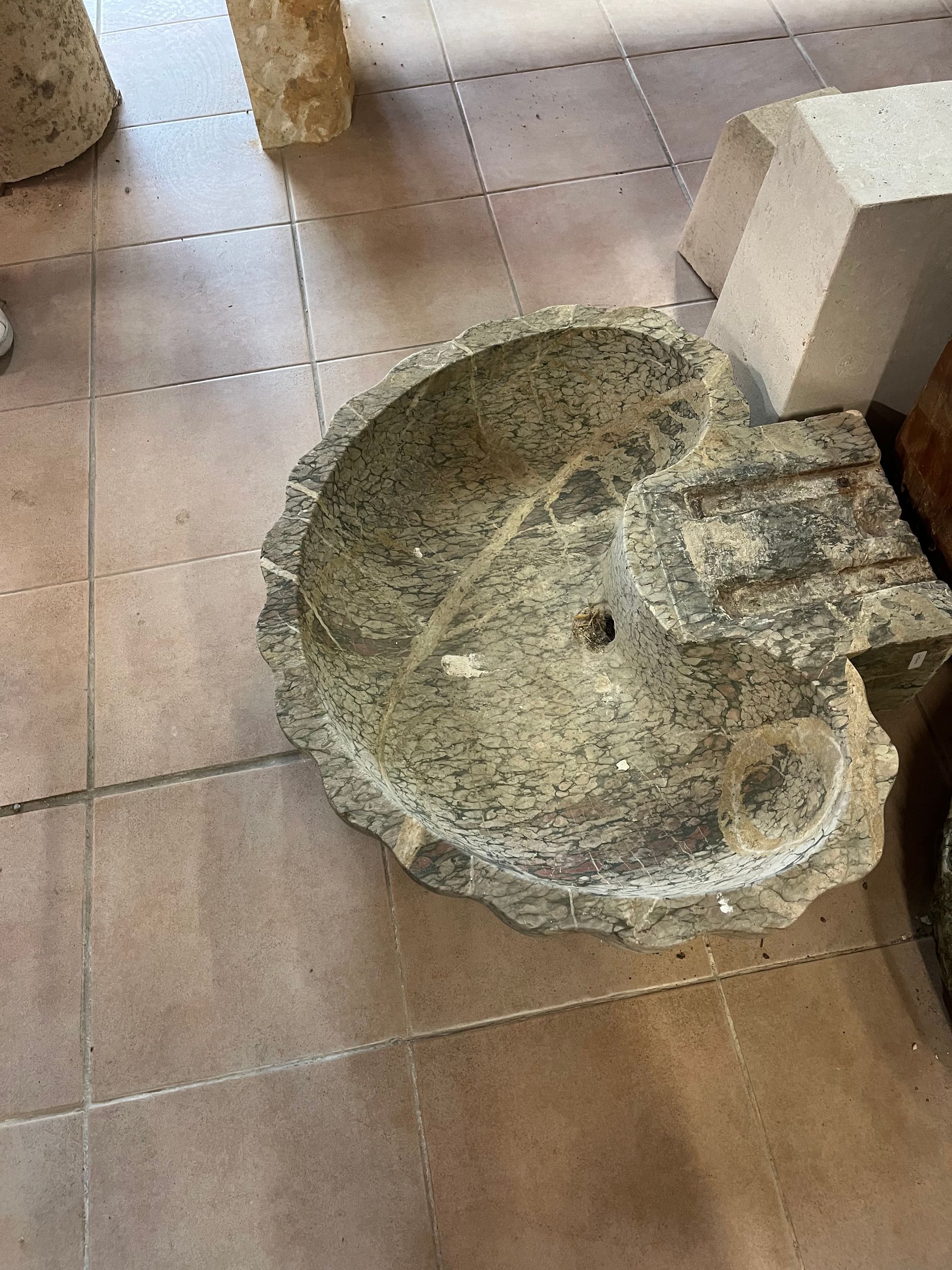 Lavabo en pierre cassée sur un sol carrelé, près d'un mur et de piliers.