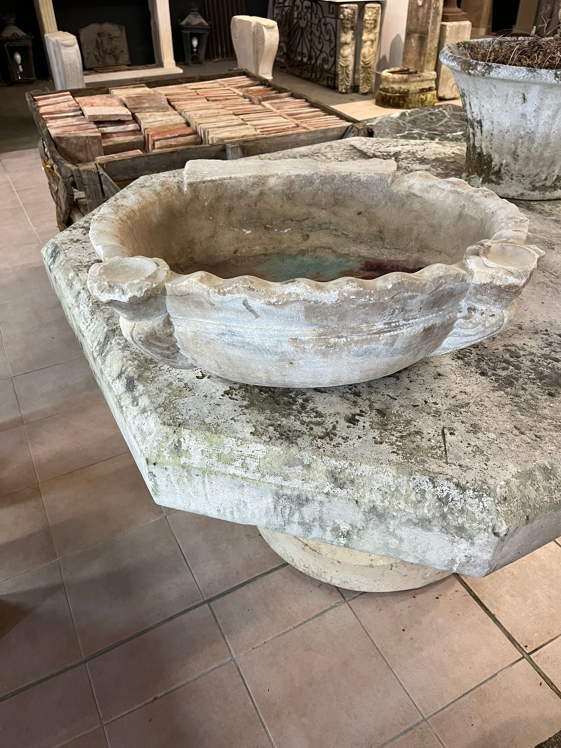 Fonts baptismaux en pierre dans une église, avec un bassin circulaire rudimentaire sur un sol carrelé.