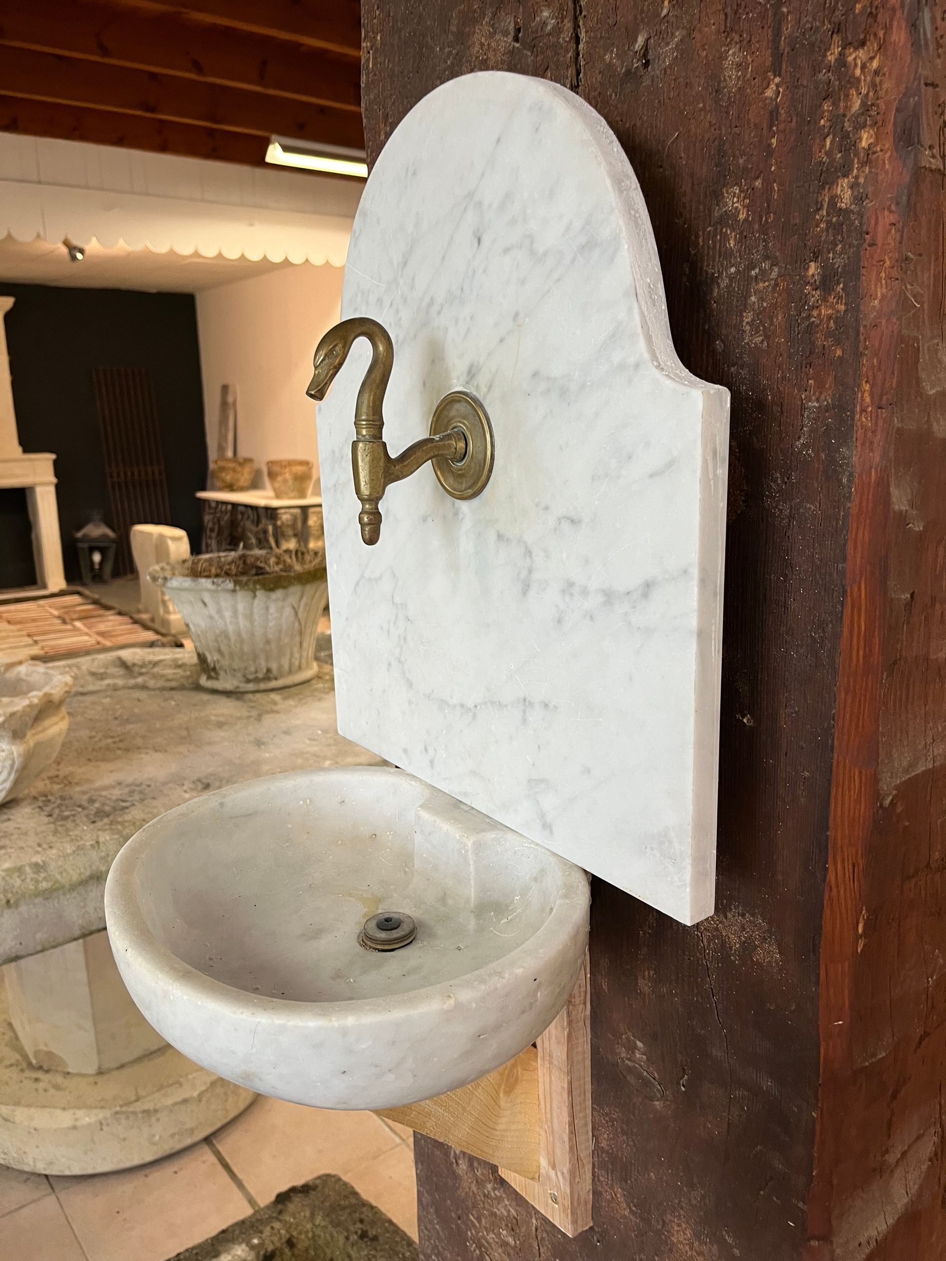 Lavabo mural rustique en pierre avec robinet en laiton et crédence cintrée blanche, à l'intérieur.