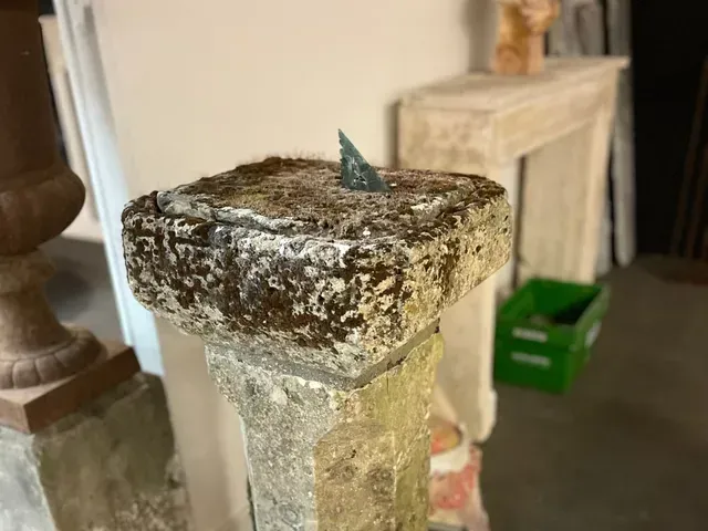 Socle en pierre patinée surmonté d'un petit objet vert, à l'intérieur, sur un sol en béton