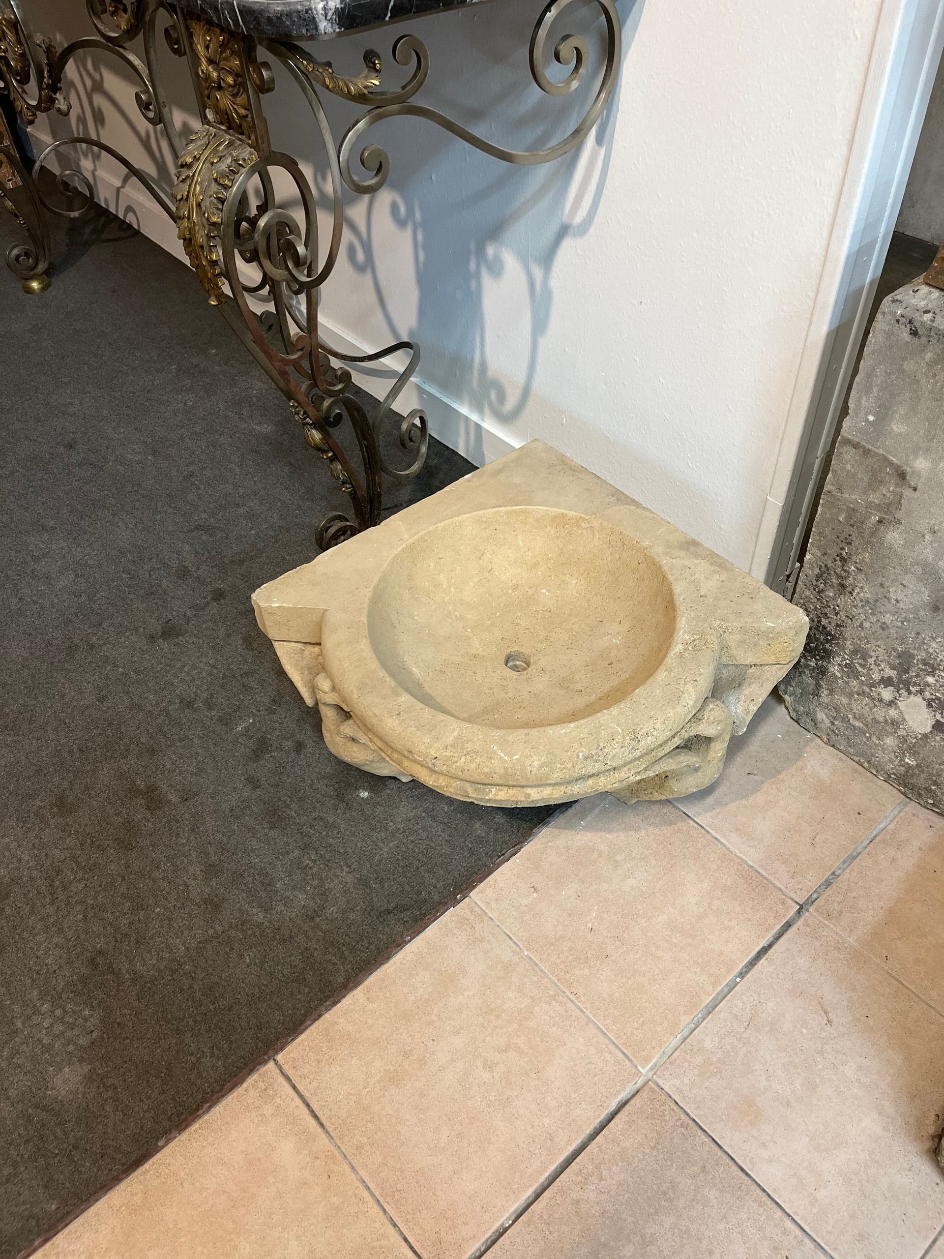 Socle en pierre pour bain d'oiseaux sur un sol carrelé, à côté d'une balustrade en métal ornée.
