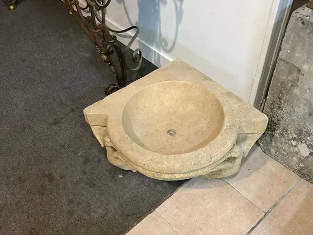 Lavabo en pierre sur un sol carrelé, près d'un mur et d'un bord de tapis.