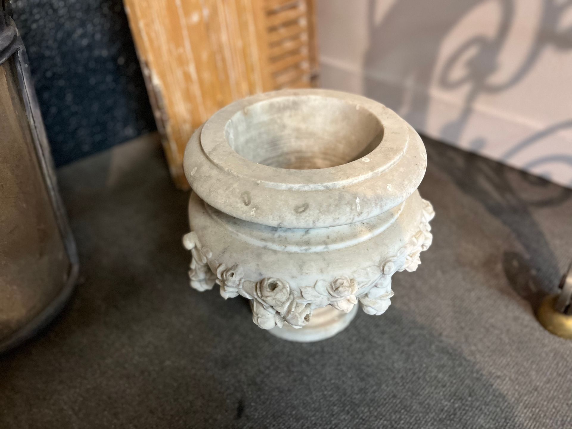 Petit pot ou bol en pierre blanche orné de motifs floraux sculptés, posé sur une table sombre.
