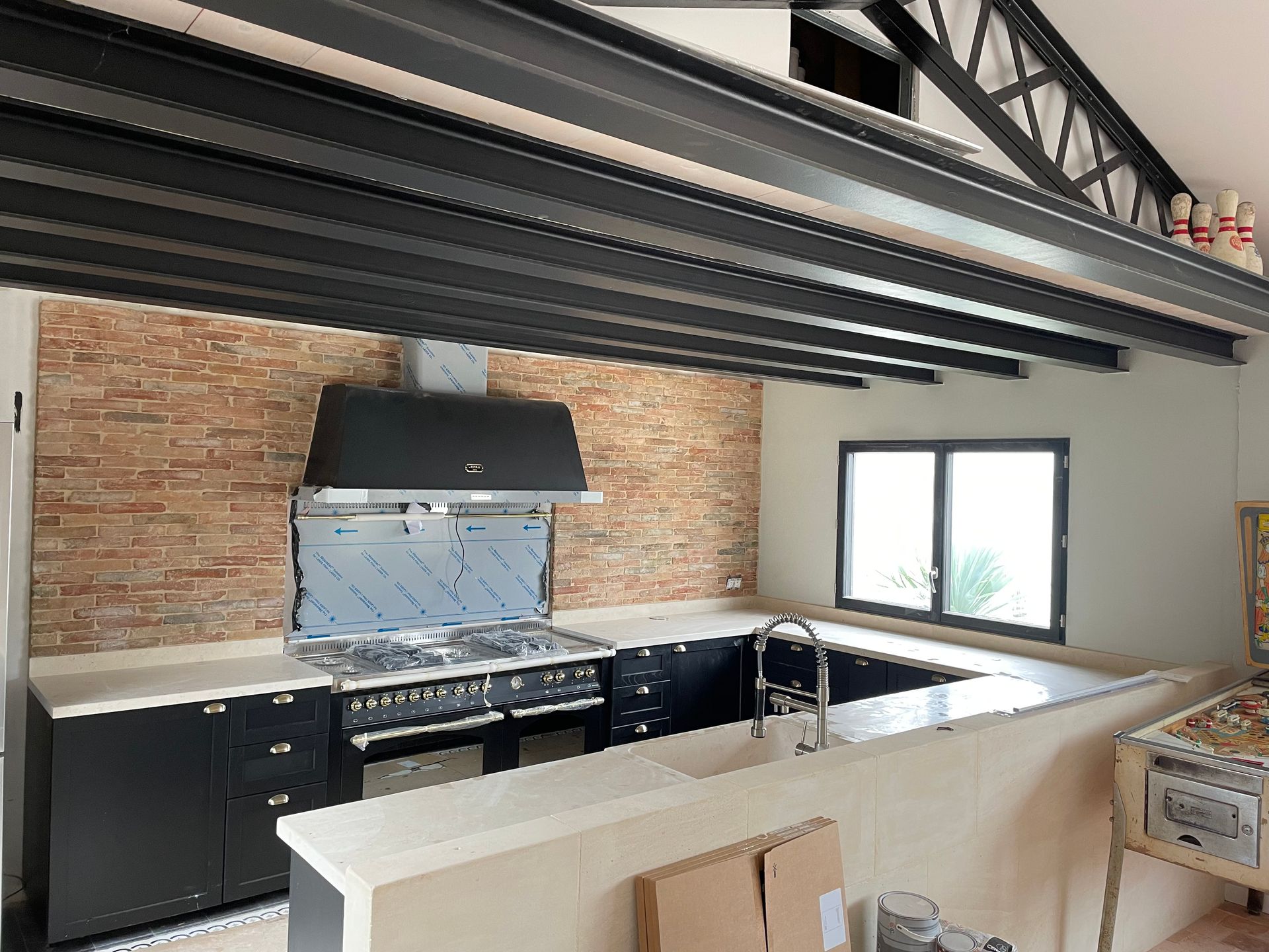 Cuisine moderne avec mur de briques apparentes, hotte aspirante noire, comptoirs blancs et grande fenêtre