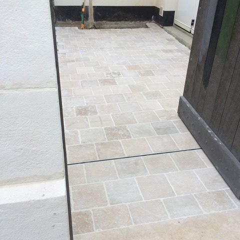 Passage étroit carrelé avec une porte à droite et un mur blanc à gauche.