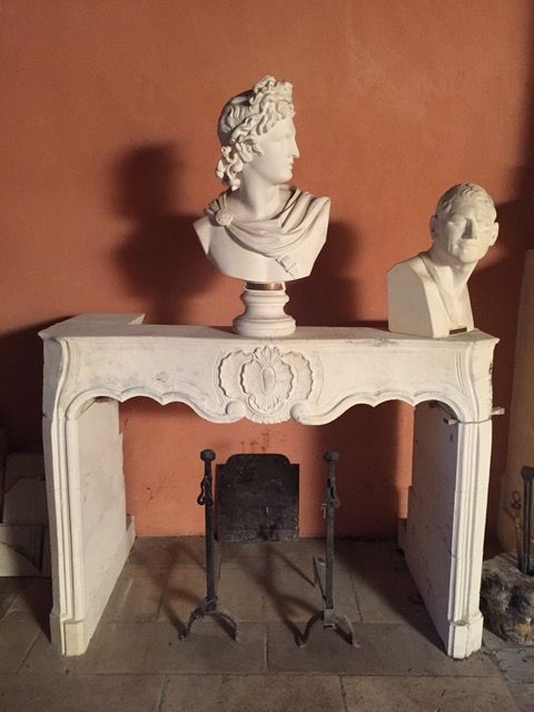 Cheminée blanche ornée de deux bustes en plâtre et d'une petite façade de cheminée noire, le tout adossé à un mur rougeâtre.