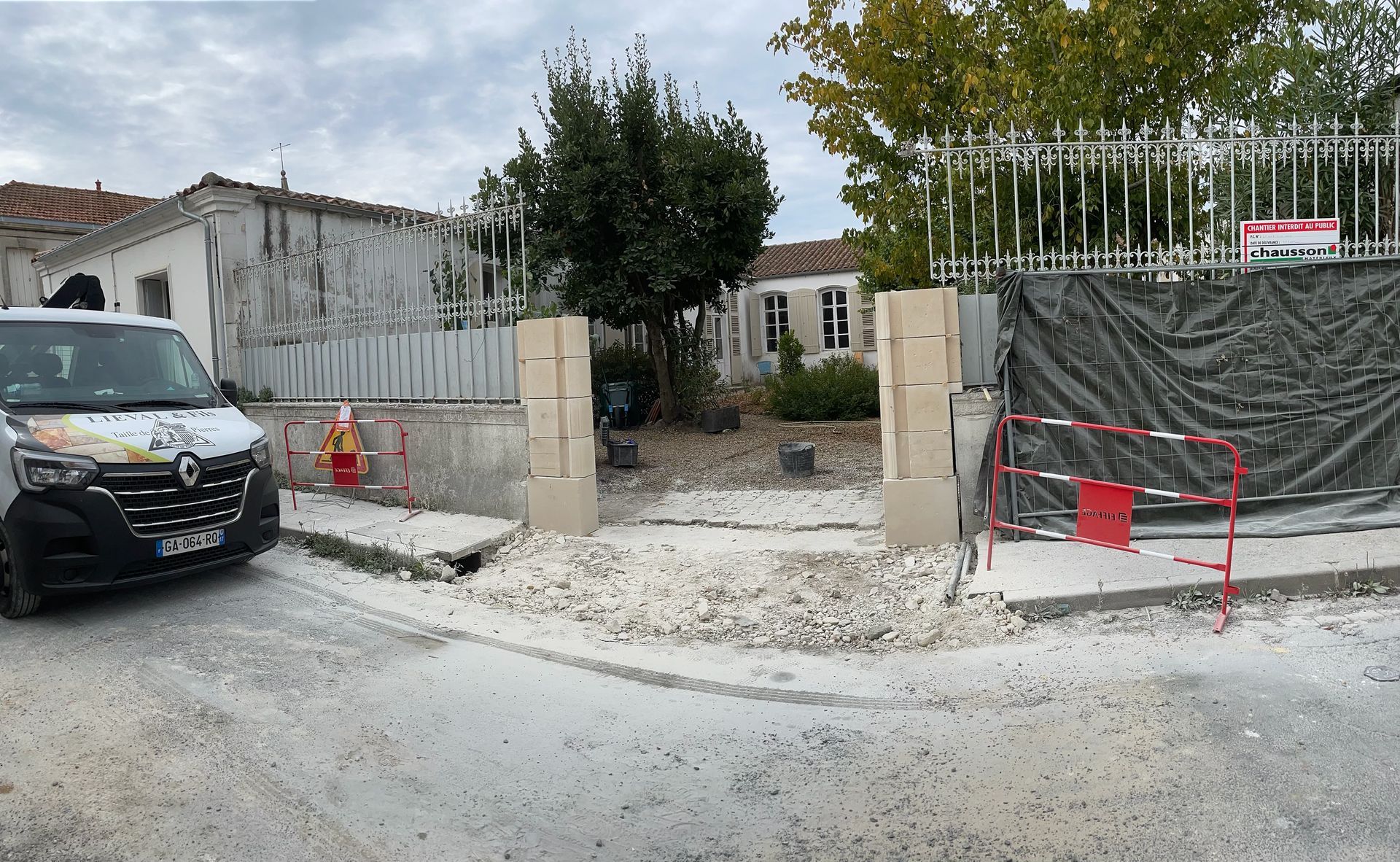 Entrée de chantier avec murs en béton, voiture noire à gauche et barrières rouges près d'un portail blanc