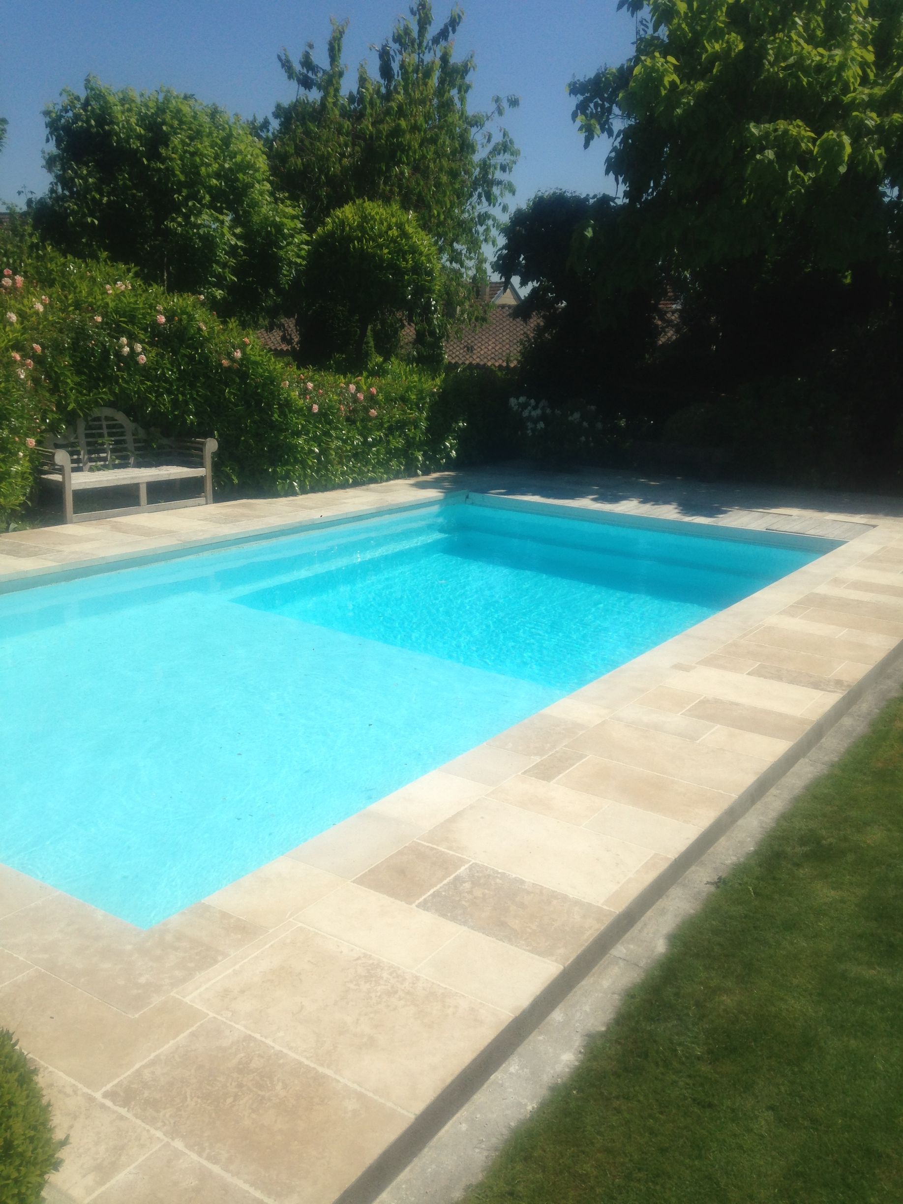 Piscine dans le jardin avec eau turquoise, terrasse en pierre, banc et arbres verdoyants