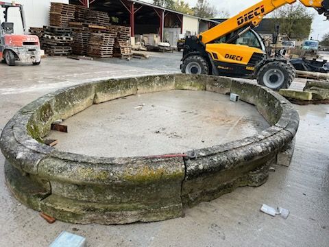 Grand bassin circulaire en béton, ou anneau, sur le sol d'un entrepôt, à côté d'un chariot élévateur JCB jaune et de palettes empilées.